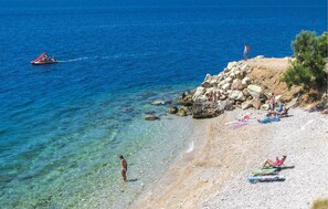 A beach with clear water, a rocky shoreline, and people enjoying the sun.