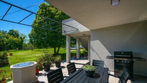 Terrassa exterior amb taula i cadires, una barbacoa i plantes en testos.