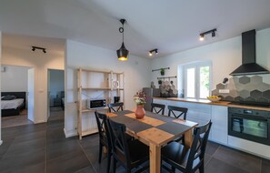 Et moderne køkken med spiseplads, indbygget ovn og et vindue med udsigt til grønne omgivelser.