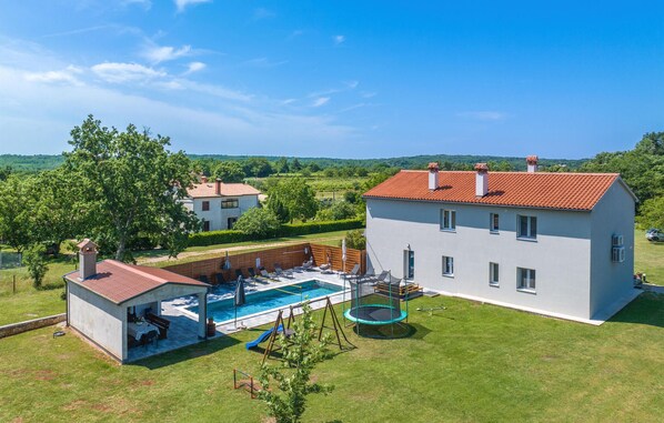 En stor bolig med swimmingpool, et separat anneks med grillområde og en velholdt græsplæne.