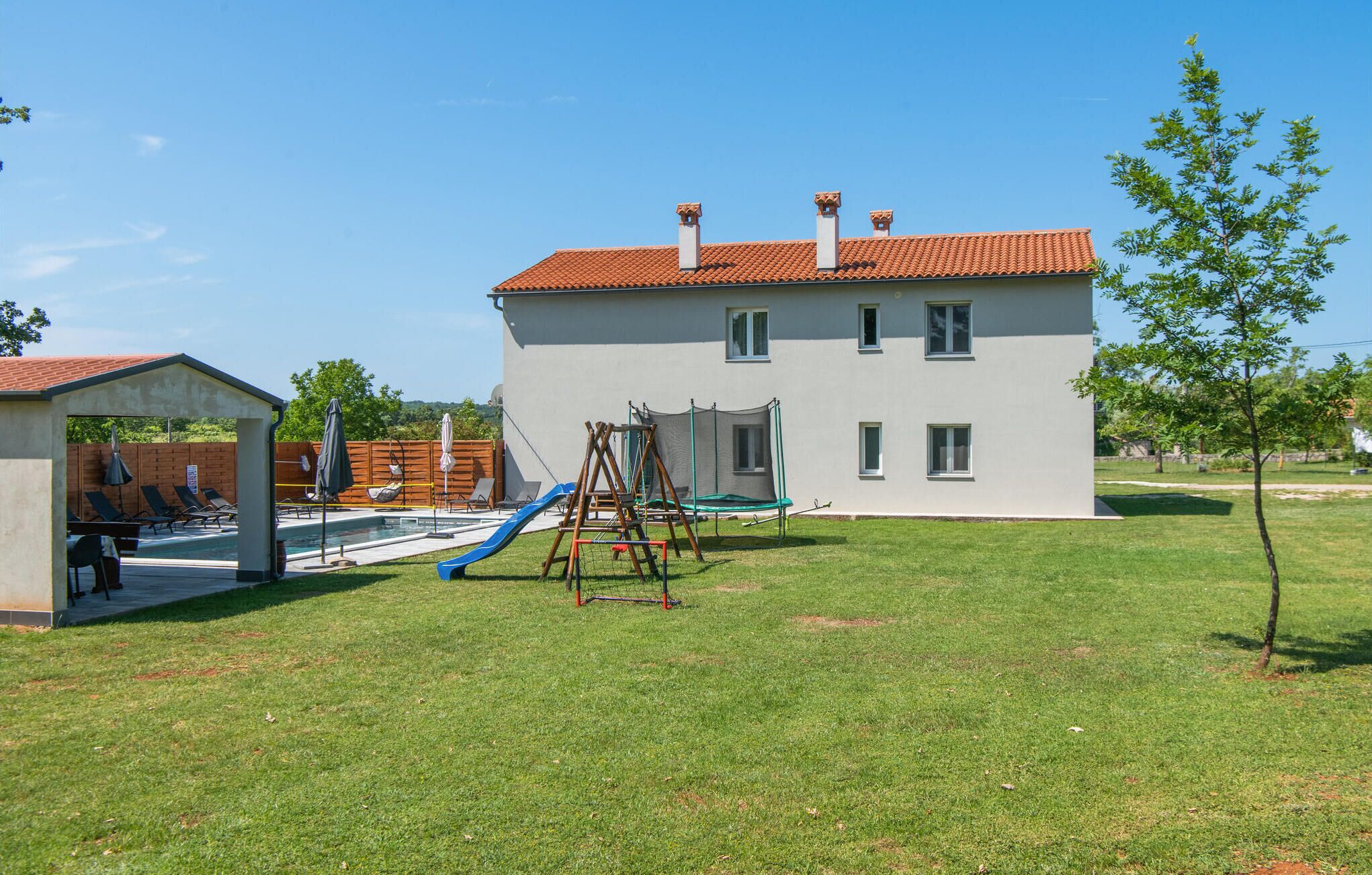 A two-story building with a red-tiled roof, a small pool area with lounge chairs, and a swing set.