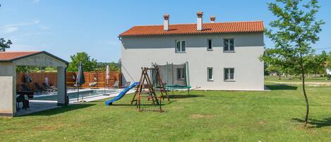 A two-story building with a red-tiled roof, a small pool area with lounge chairs, and a swing set.