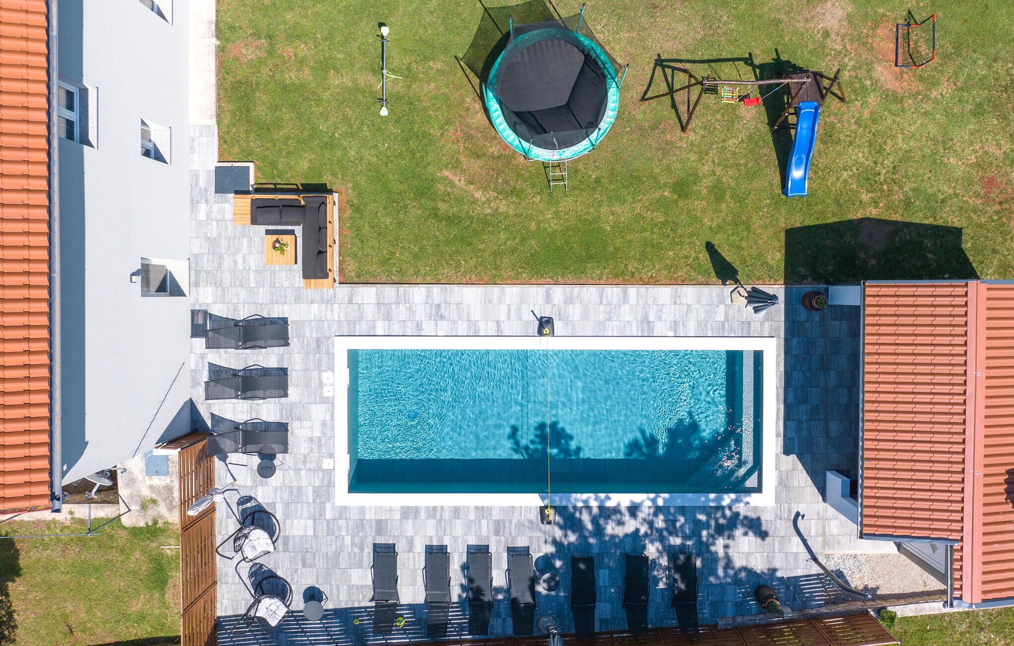 Vue aérienne d’une propriété résidentielle dotée d’une piscine, d’un trampoline et d’un toboggan.