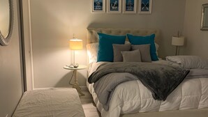 Un dormitorio con cama, mesita de noche, lámpara y un banco.