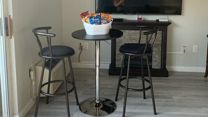Un comedor con una mesa redonda y dos sillas, un bol de aperitivos, un televisor de pantalla plana y una chimenea.