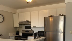 Una cocina moderna con armarios blancos, un refrigerador de acero inoxidable, horno empotrado y un reloj en la pared.