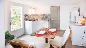 Ett kompakt kök med vita skåp, kakel ovanför arbetsbänken och en matplats med ett träbord och stolar.