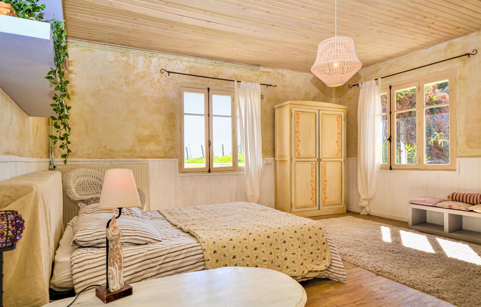 Un dormitorio con cama, mesita de noche, lámpara, armario y ventanas.