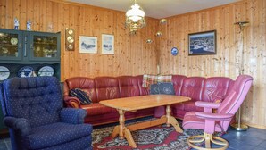 Et hyggeligt rum med en væg af træpaneler, en rød lædersofa, en blå lænestol, et træbord og en lysekrone.