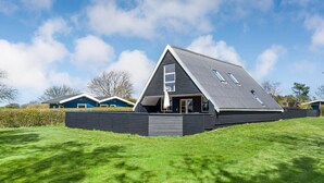 Une maison moderne avec un toit en pente, une fenêtre de grenier bien visible et une pelouse bien entretenue.