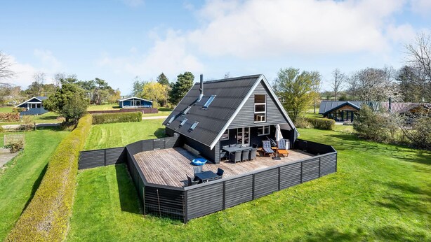 Une maison moderne dotée d’une grande terrasse, entourée d’une pelouse bien entretenue et d’arbres.