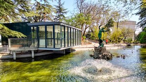 Eine Glaskonstruktion überspannt einen Teich mit einer Statue einer Figur auf einem Felsen.