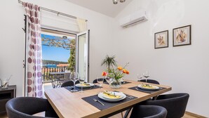 A dining area with a wooden table, black chairs, and a view of the sea through a glass door.