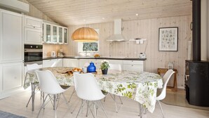 Una cocina moderna con armarios blancos, una isla central con sillas, un techo grande de madera y una estufa negra.