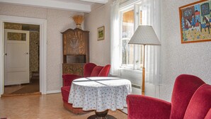 Una habitación con una mesa cubierta por un mantel floral, sillas rojas, un aparador de madera y una lámpara.