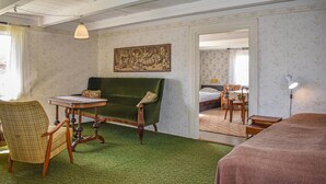 Una habitación con sofá verde, una silla de madera, una mesita, una cama y un cuadro en la pared.
