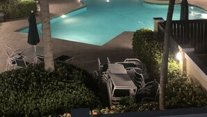 A nighttime view of a swimming pool surrounded by palm trees and lounge chairs, with a building in the background. - Breathtaking Oceanview Villa in Paradise (HUMACAO)