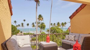 A balcony with wicker furniture, a red lantern, and a view of the beach and palm trees. - Breathtaking Oceanview Villa in Paradise (HUMACAO)