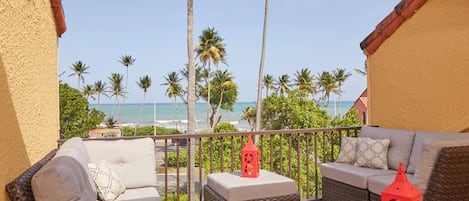 A balcony with wicker furniture, a red lantern, and a view of the beach and palm trees.