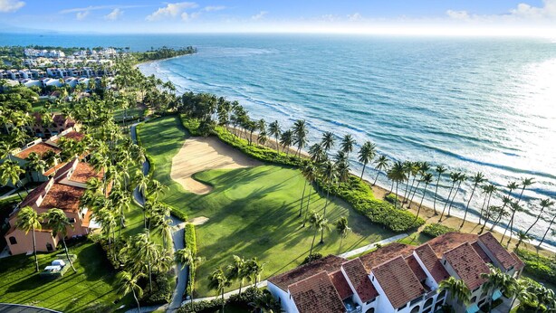 A golf course with a view of the ocean and a residential area with palm trees and buildings. - Breathtaking Oceanview Villa in Paradise (HUMACAO)