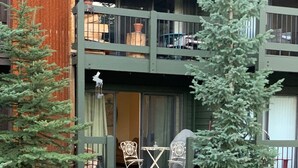 A two-story building with a balcony, outdoor seating, and a small tree.