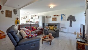 Sala de estar con sofá, sillón y mesa de centro. Se observa una cocina al fondo.