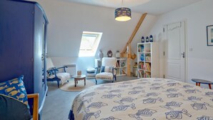 Un dormitorio con techo inclinado, una cama con colcha estampada de peces, una estantería, una ventana y un armario.