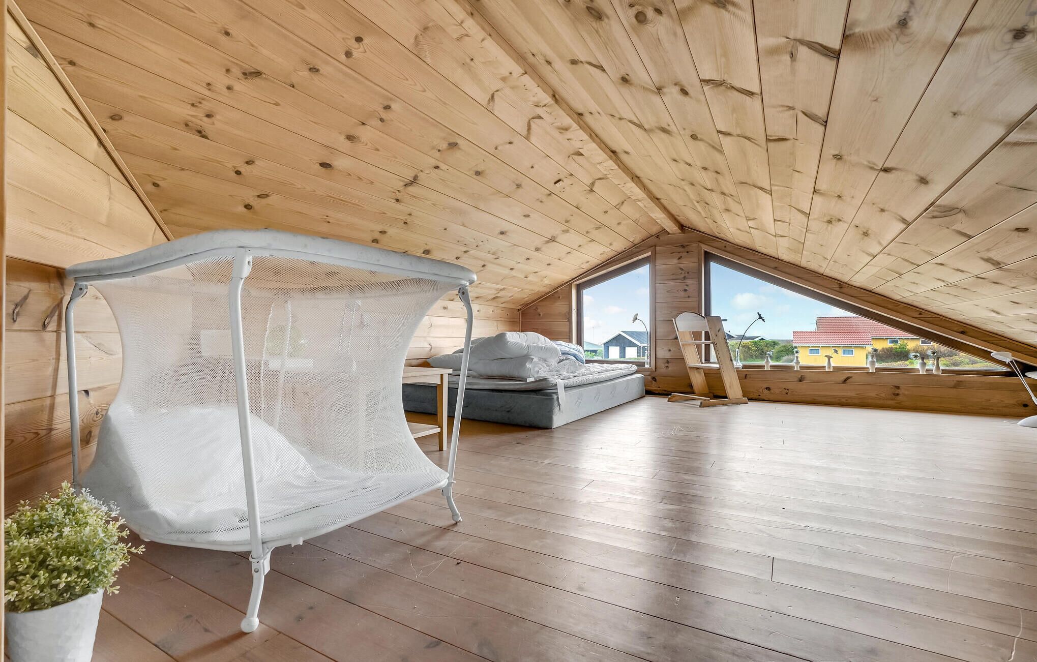 A spacious attic bedroom with a large window, a bed, a white canopy chair, and a view of the outside.