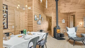 Viehättävä puinen mökki, jossa on ruokailutila, pieni pöytä kahdelle, takka ja mukava nojatuoli.