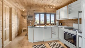 Moderni keittiö, jossa on puuseinät, valkoiset kaapit ja suuri ikkuna, josta avautuu näkymä ulos.