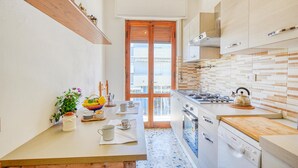 A compact kitchen with a stove, oven, and sink. There is a wooden countertop and a tiled backsplash. A window with a view of balconies is visible. - Awesome apartment in Viareggio with WiFi (Viareggio)