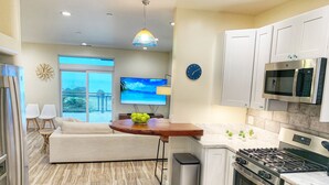A modern kitchen with white cabinets, a stainless steel stove, and a microwave. There is a dining area with a wooden table and chairs, and a TV mounted on the wall. - ★★★★ Brand New Beautiful Ocean View Home ★★★★ (Whitethorn)