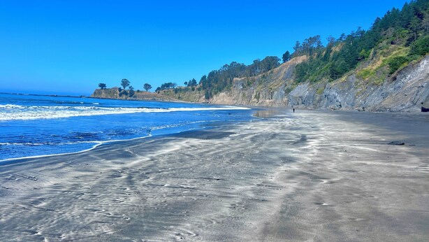 A beach with a clear sky, waves, and a forested hillside. - ★★★★ Brand New Beautiful Ocean View Home ★★★★ (Whitethorn)