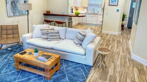 A modern living room with a sofa, coffee table, and a dining area with a kitchen in the background. - ★★★★ Brand New Beautiful Ocean View Home ★★★★ (Whitethorn)