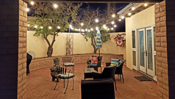 An outdoor patio area with brick flooring, a covered seating area with chairs and tables, string lights, and a tree. - Close to downtown but feels like country-Very Private! Refreshing pool & hot tub (Tucson)
