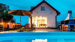 A house with a swimming pool, outdoor seating, and a well-lit entrance.