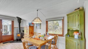Un coin repas chaleureux avec une table et des chaises en bois, un buffet vert et un poêle à bois.