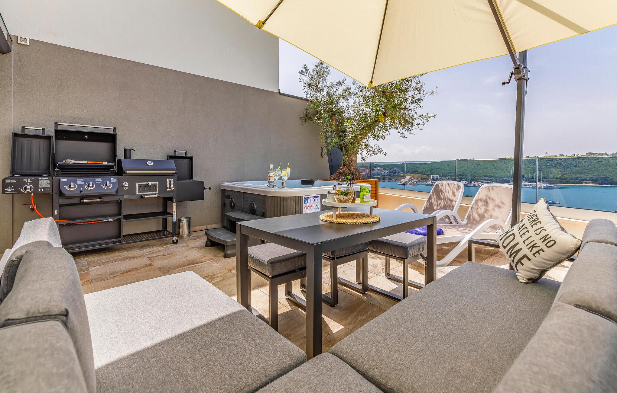 An outdoor patio with a grill, seating area, and a view of the sea.