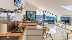 Uma cozinha moderna com vista para o mar, uma sala de jantar com mesa e cadeiras, e uma sala de estar com sofá e televisão.