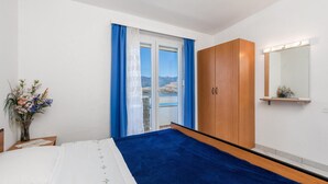 Une chambre à coucher avec un lit, une armoire en bois, un miroir et une vue sur un lac, visible à travers une fenêtre ornée de rideaux bleus.