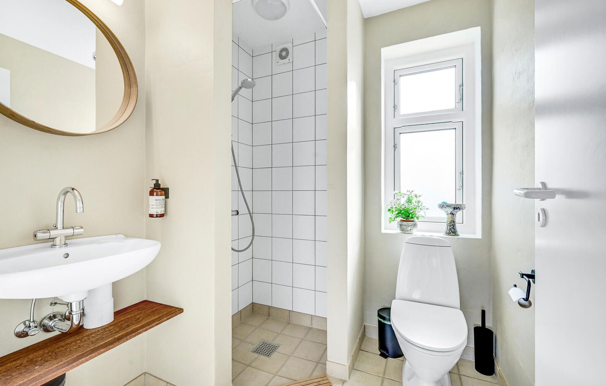 A bathroom with a white sink, a shower with a grid-patterned wall, a toilet, and a window with a plant.