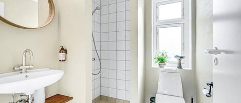 A bathroom with a white sink, a shower with a grid-patterned wall, a toilet, and a window with a plant.