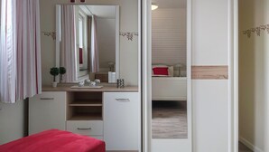 A bedroom with a red bed, a bedside table with a lamp, a mirror, and a dresser with a plant. - 5 bedroom amazing home in Wurster Nordseeküste (Wurster Nordseeküste)