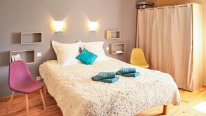 Una camera da letto con un letto bianco soffice, due luci a parete, un pavimento in legno, una poltrona viola e una gialla.
