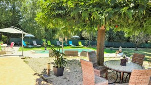 Un giardino sul retro con piscina, lettini e un tavolo con sedie.