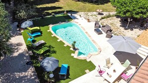 Una piscina rettangolare con un solarium circostante, diverse poltroncine e ombrelloni.
