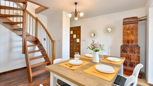 Un comedor con mesa de madera dispuesta para cuatro personas, una escalera de madera y un adorno en la pared.