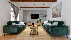A modern living room with two green sofas, a wooden coffee table, a flat-screen TV mounted on the wall, and a large floral painting. - Nice home in Lisicic with sauna (Lisicic)