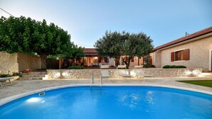 A swimming pool with a stone deck, surrounded by a stone wall and a brick building with wooden shutters. - Nice home in Lisicic with sauna (Lisicic)
