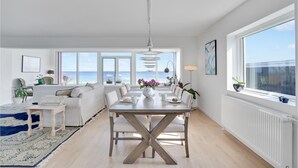 Un vaste espace de vie comprenant une table à manger, des canapés et une vue sur la mer.